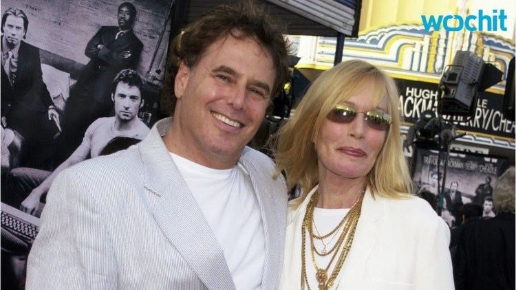 Jonathan D. Krane and Sally Kellerman are smiling. Jonathan is wearing a light gray coat over a white shirt while Sally with blonde hair, wearing sunglasses, a gold necklace, and a white long sleeve top.