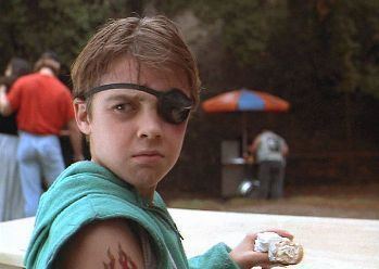 Jordan Christopher wearing an eye patch while eating in a movie scene from "Motorama (1991)"