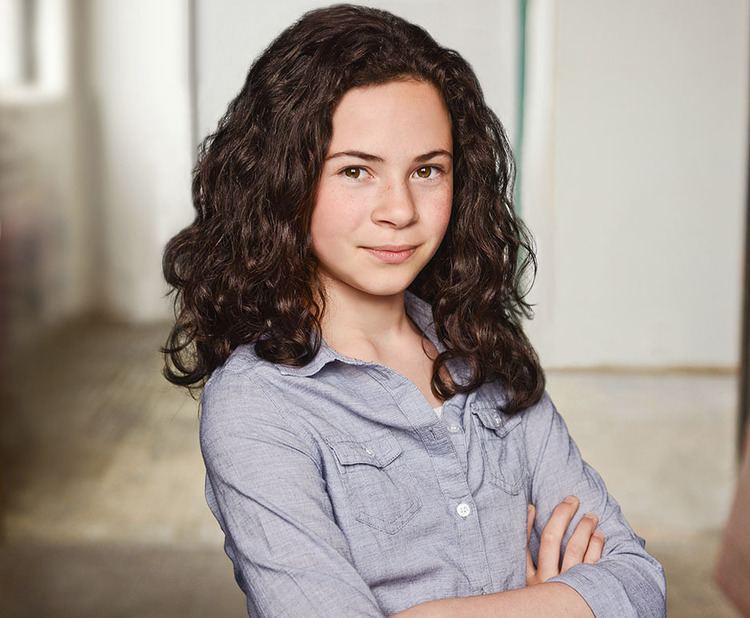 Jordyn Negri smiling with her curly hair down and crossed arms while wearing a gray collared long sleeve.