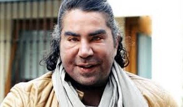 Jorge Kahwagi smiling with long hair and a fatter face and wearing a yellow jacket and a white scarf.