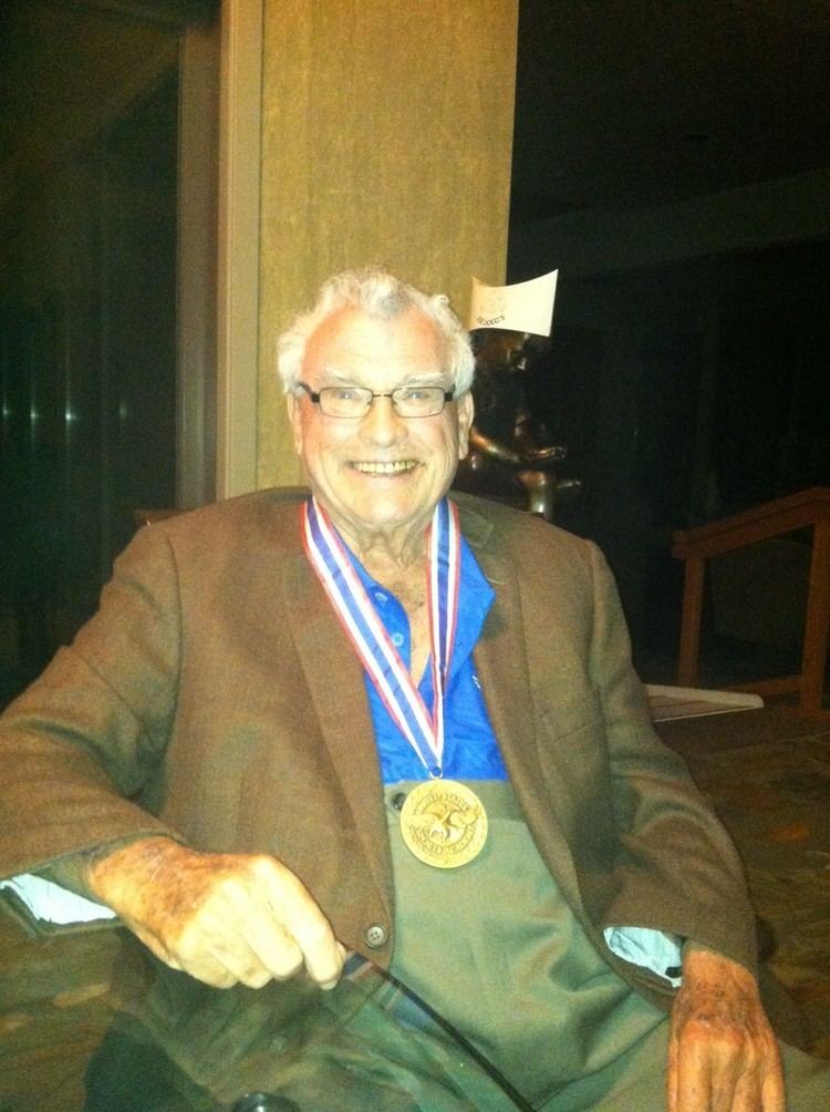 Joseph A. Hardy III wearing eyeglasses, brown coat, blue long sleeves and medal while smiling