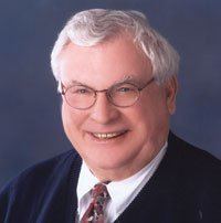 Joseph A. Hardy III wearing eyeglasses, black coat, white long sleeves and neck tie while smiling