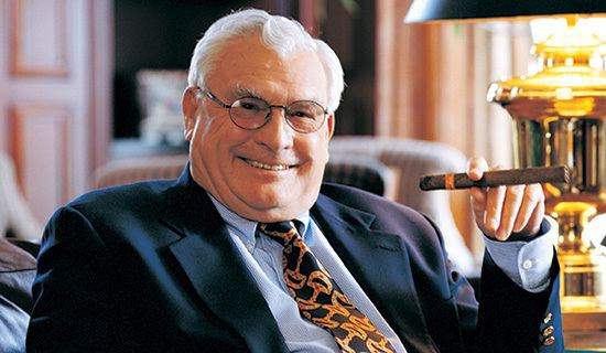 Joseph A. Hardy III wearing black coat, light blue long sleeves and neck tie while holding tobacco