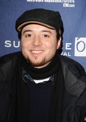 Joseph Perrino smiling while attending the screening of "Assassination of a High School President" at Eccles Theatre during the 2008 Sundance Film Festival. Joseph with a beard is wearing a cap, a white shirt under a blue shirt with a checkered collar, a black scarf, and a black jacket.