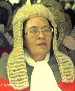 Joyce Bamford-Addo with her serious look wearing a pair of eyeglasses, and a white and gray colored shirt