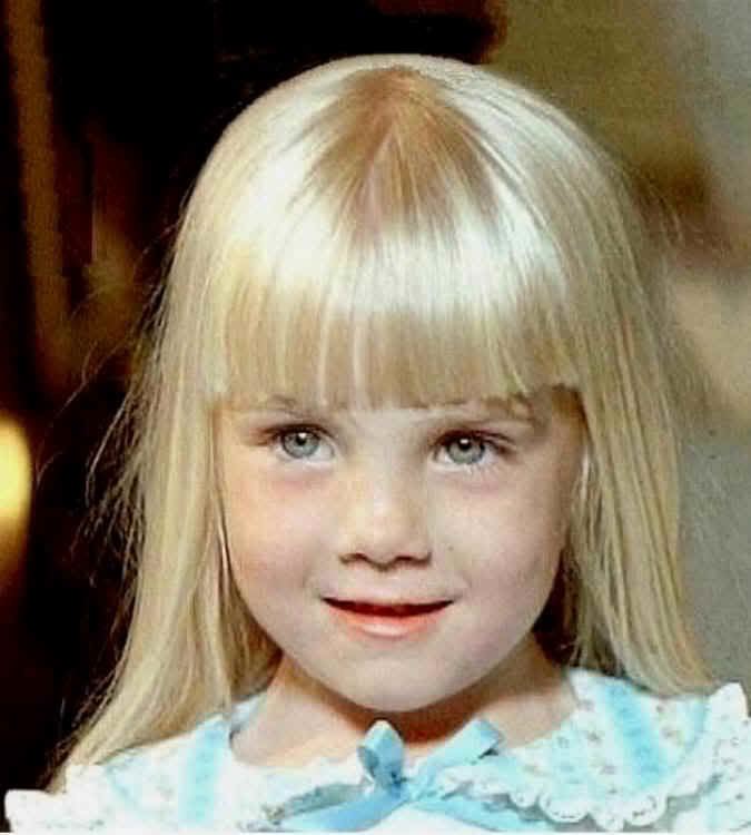 Heather O'Rourke smiling, with blonde hair and wearing a light blue dress.