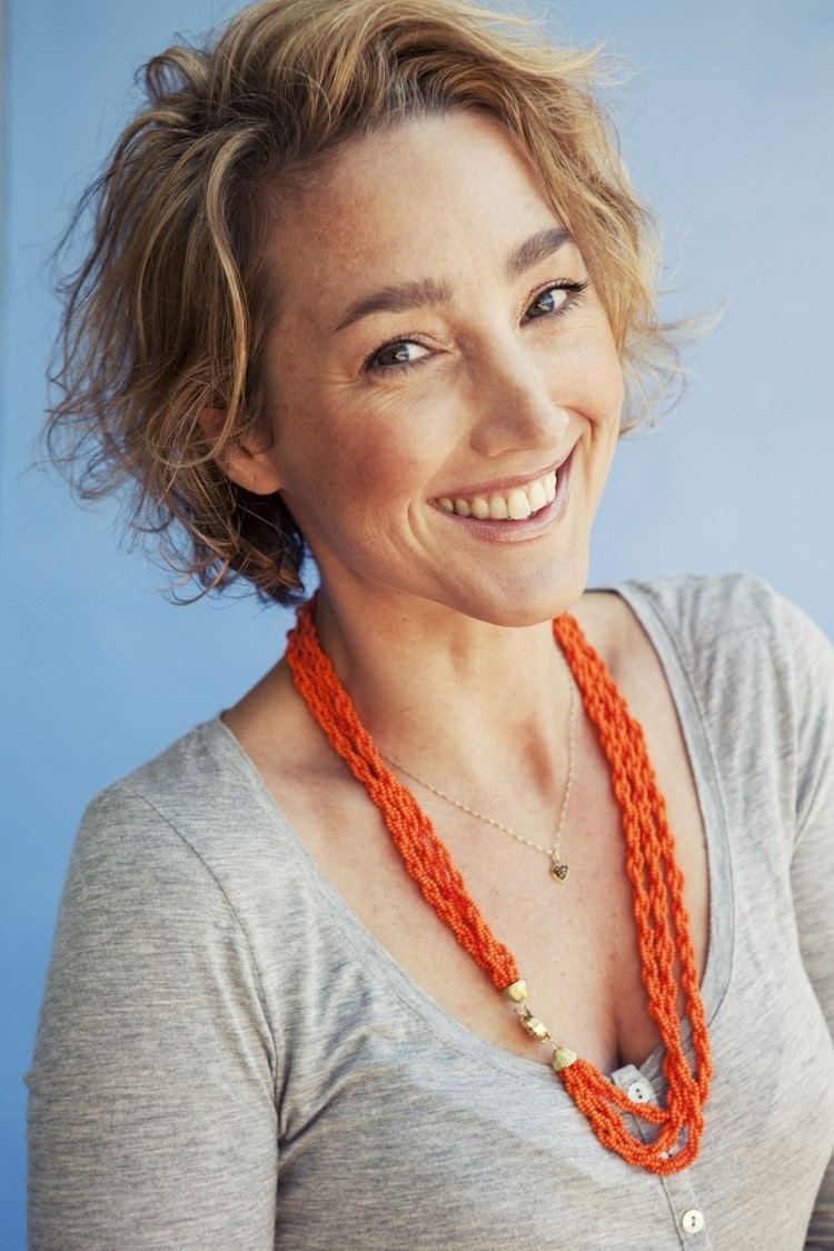 Judith Anna Pronk wearing a gray shirt and a necklace with short curly blonde hair.