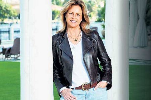 Judy Nelson smiling and wearing black leather jacket, white top and jeans