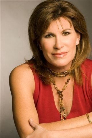 Judy Norton with blonde hair, wearing a necklace, a bracelet, and a sleeveless red top.