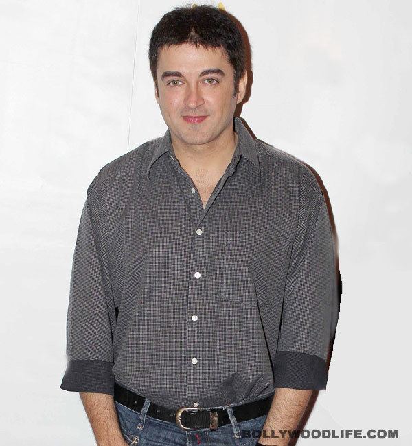 Jugal Hansraj smiling while wearing black and gray long sleeves, black belt, and jeans