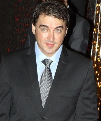 Jugal Hansraj wearing a black coat, light blue long sleeves and gray necktie