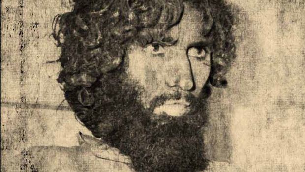 Juhayman al-Otaybi with a sad face, curly hair, a mustache, and a thick beard.