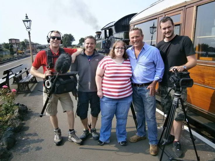Jules Hudson smiling with his wife Tania and other staff on his program. Jules wearing light blue long sleeves and blue pants while Tania wearing a white and red striped shirt and blue pants.