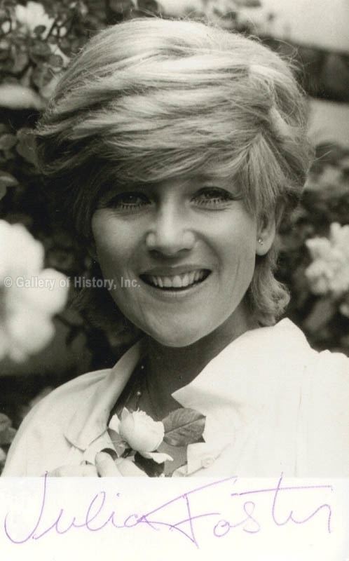 Julia Foster smiling while holding a flower and wearing a white blouse