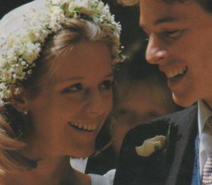 Julia and James Ogilvy are smiling and looking at each other during their wedding. Julia wearing a floral headdress and white gown while James wearing a black coat.