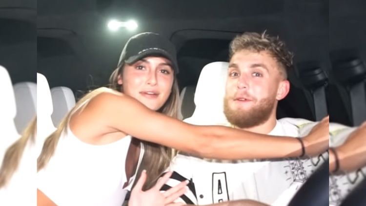 Julia Rose and Jake Paul are smiling. Julia wearing a black cap and both are wearing white shirts.