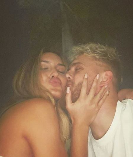 Jake Paul kissing Julia Rose on the cheek while Julia holding his face. Julia with long blonde hair while Paul wearing a white shirt.