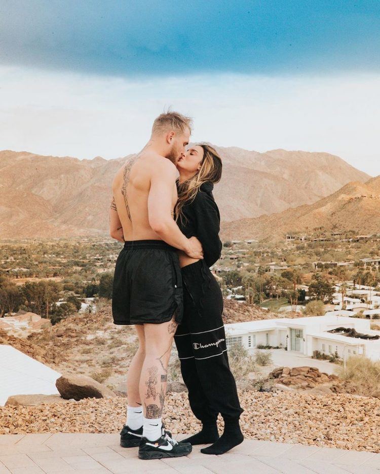 Jake Paul and Julia Rose doing an intimate kiss. Julia wearing an all-black outfit while Paul wearing black shorts, black shoes with white socks.