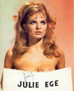 Julie Ege topless while holding a placard with her name on it, with a serious face while looking above and with wavy blonde hair,