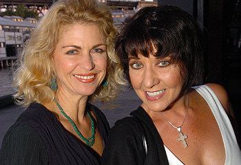 Julieanne Newbould with a smiling face and blonde hair, wearing a necklace and a black shirt with a lady wearing a necklace and a white top.