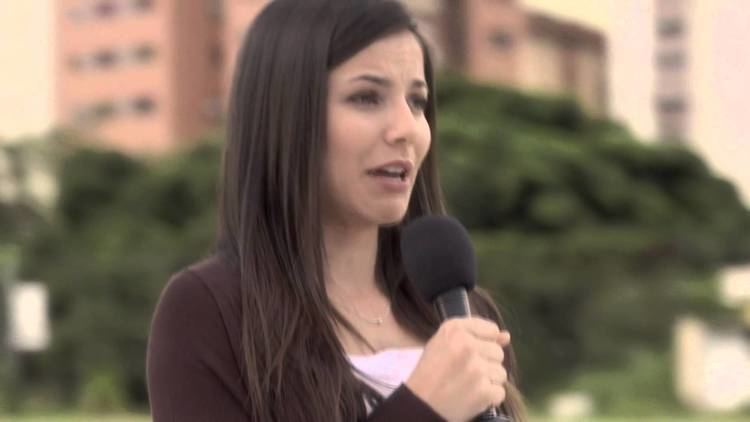 Juliette Pardau singing while holding a microphone and wearing a white and brown blouse