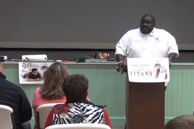 Julius Campbell standing on the podium while wearing a white shirt in front of many people