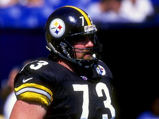 Justin Strzelczyk looking afar with mustache and beard while wearing a black and yellow football helmet and number seventy-three black and yellow jersey