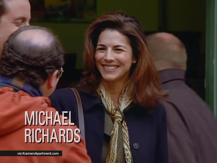 Justine Miceli smiling while wearing a blue blazer and white and brown scarf