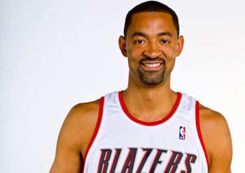 Juwan Howard smiling with a beard and mustache while wearing a red and white jersey with the word "BLAZERS" and the NBA logo written on it
