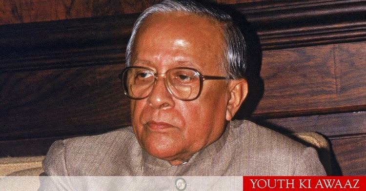 Jyoti Basu while sitting on a chair wearing a brown long-sleeved shirt and pair of eyeglasses