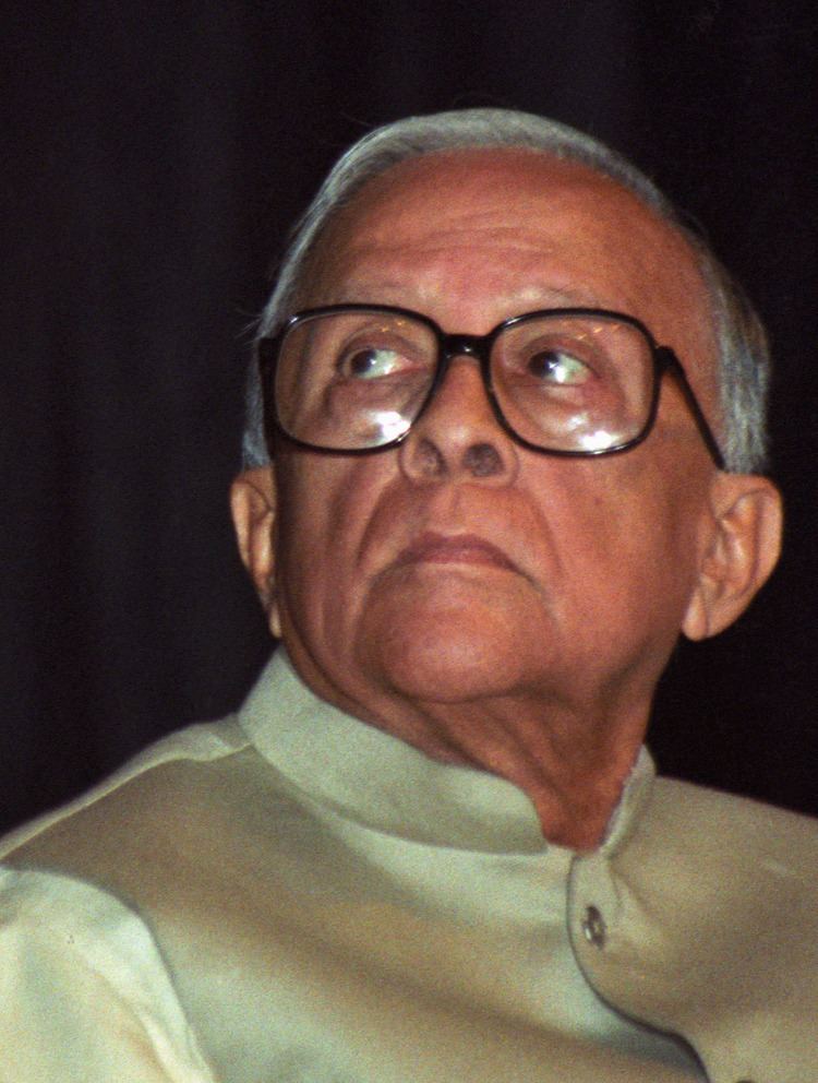 Jyoti Basu looking upward wearing a white long-sleeved shirt and eyeglasses