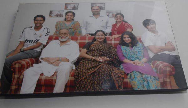 K. Balaji wearing white long sleeves, white pants and eyeglasses while sitting on a couch with his family