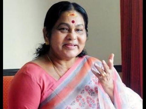 K. P. A. C. Lalitha smiling while talking to someone and wearing a pink blouse, blue and pink dupatta, necklace, and earrings