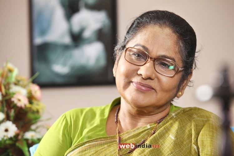 K. P. A. C. Lalitha with a tight-lipped smile while wearing an apple green blouse, green dupatta, eyeglasses, earrings, and necklace