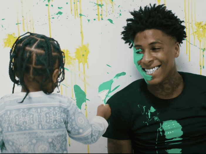Back of Kacey Alexander Gaulden with braided hair with his father Kentrell DeSean Gaulden smiling, with paint on his face and wearing a black shirt with paint.