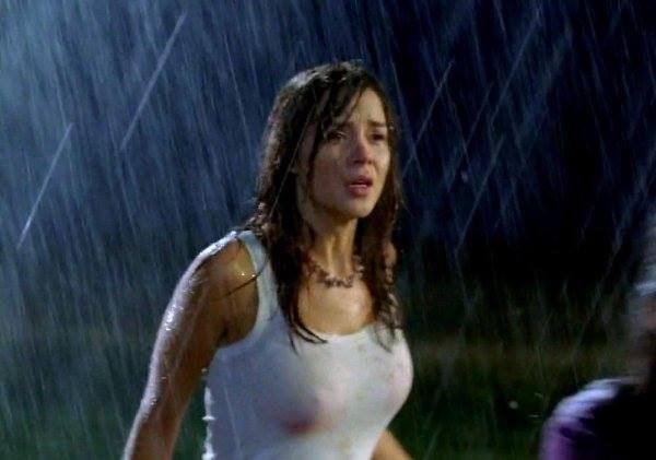 Kacey Clarke seriously looking at someone while raining with her hair down a wearing a necklace and a see-through white sleeveless.