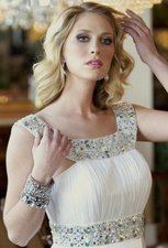Kaitlynne Postel with a fierce look while touching her wavy blonde hair, wearing bracelets, and a white sleeveless dress.