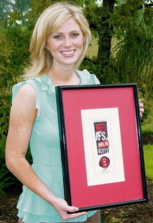 Kaitlynne Postel smiling while holding a frame, with blonde hair, and wearing a mint green sleeveless dress.