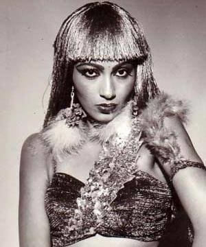 Kalpana Iyer with a fierce look while wearing a wig, dangling earrings with feathers, an armlet, and a sleeveless top with feathers