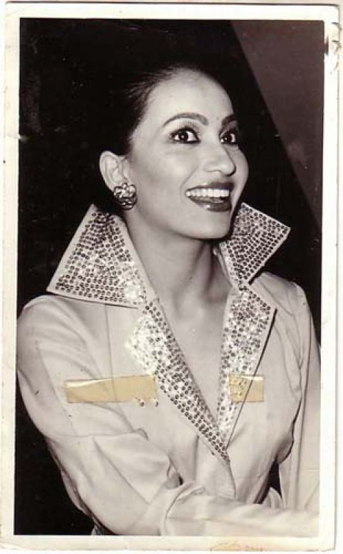 Kalpana Iyer smiling while looking at something and wearing earrings and a coat with sequins on the collar