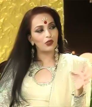 Kalpana Iyer looking and talking with someone, with long black hair, a red and gold Bindi on her forehead while wearing a nose jewel, dangling earrings, and a cream long sleeve saree