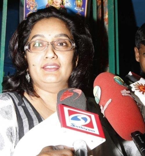 Kanaka smiling during an interview while wearing a black and white blouse and eyeglasses