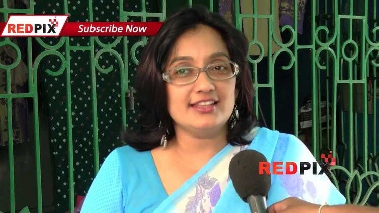 Kanaka smiling during an interview while wearing eyeglasses and a blue dress