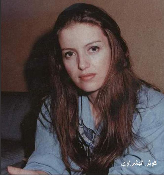 In a room with brown walls, Kaouthar Bachraoui is serious, sitting on a black couch, she has long brown hair wearing a blue denim jacket.