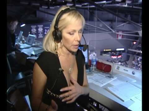 In a room with a long white table with laptops and papers on top and a glass window with a view of the ice rink where sportscasters stationed, from left a man is sitting, looking at the laptop, has black hair and a beard wearing black top and black pants, at the right is Karen Newman is serious, sitting with her left hand over her chest, has blond hair with black headphone on top, wearing a hoop earrings a gold necklace and a black cleavage showing shirt.