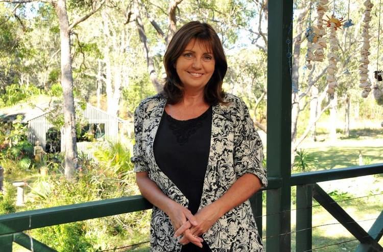 Karen Pini smiling and wearing black and white coat and black inner top while trees in the background