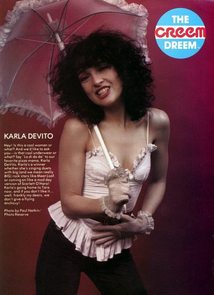 A magazine cover featuring Karla DeVito smiling while holding a white lace umbrella, with curly hair, wearing a white spaghetti top with a plunging neckline, white gloves, and black pants.