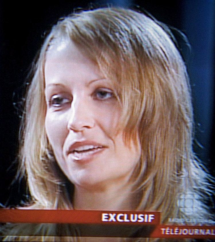 Karla Homolka is serious, mouth half open, looking to her right. in black background, has blonde hair middle-length hair, at the bottom is a word written “EXCLUSIF TElEJOURNAL”