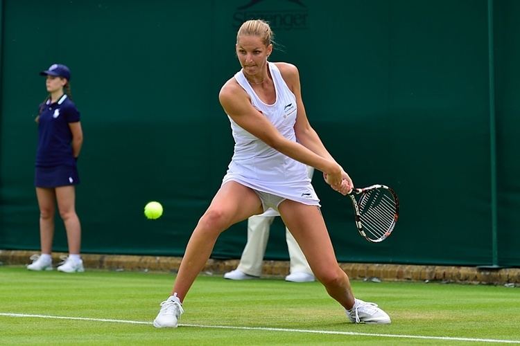 Karolína Plíšková wearing a white sleeveless top, white skirt, and white shoes while playing tennis.