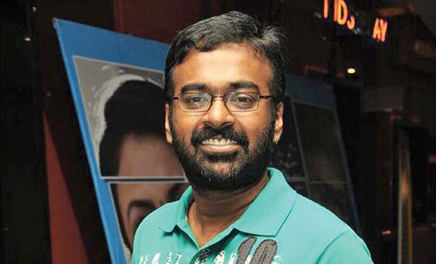 Karu Pazhaniappan smiling while wearing eyeglasses and blue-green polo shirt